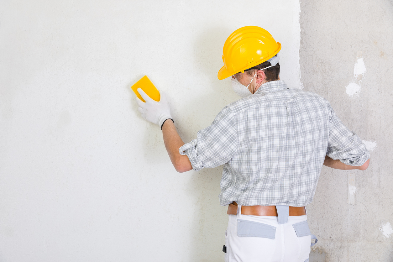 Builder sanding and smoothing newly plastered wall for professional painting in the San Ramon area